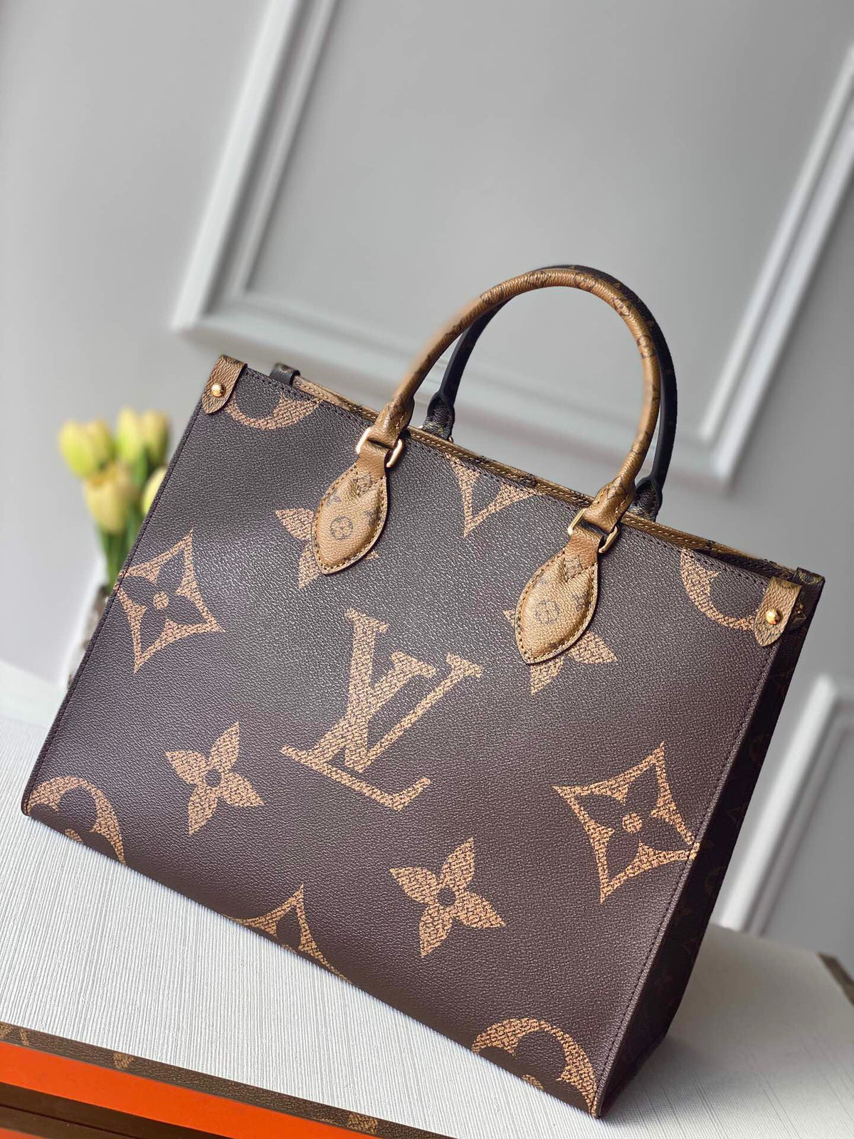 Brown top-handle tote with oversized monogram print and contrasting patterned handles
