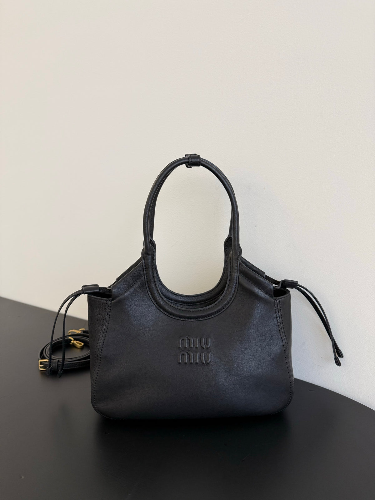 Black tote bag with oval-shaped twin handles, curved top edge and side ties